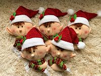 Group of five plush elf heads on a beige carpet, each wearing a red glittery Santa hat and striped scarf, showing front and side views.