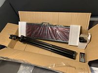 Digital countdown timer boxed with protective foam, tripod stand, remote control, and power adapter visible.