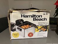 Damaged box showing Hamilton Beach deep fryer with a basket of fried food inside, highlighting adjustable timer feature and 5 year warranty.