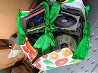 Large reusable shopping bag filled with multiple CDs in cases, all missing the front covers.