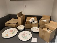Overall image showing several boxes containing Lenox dishware items including plates and cups with floral butterfly motifs.