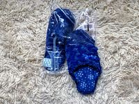 Pair of new women's blue winter slippers with fuzzy exterior and snowflake pattern, size 9-10, still in plastic packaging with tags attached, on a beige carpet.