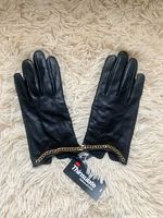 Pair of small black leather women's gloves with gold chain detail and a Thinsulate insulation tag on a cream shaggy surface.
