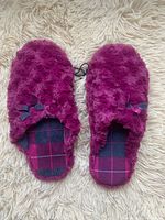 Top-down view of a pair of women's fuzzy slippers in a deep purple-burgundy color with plaid inner soles and small bows on top.
