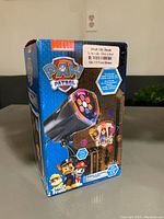 Front of original box showing Paw Patrol Christmas projector with colorful lens and branding.