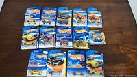 Fourteen new Hot Wheels cars displayed on a table in original blue packaging.
