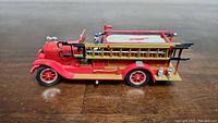 Side view of the red 1928 fire truck model showing ladders on side, coiled hose on top, and firefighter figure