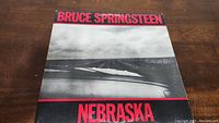 Front cover of Bruce Springsteen Nebraska vinyl showing monochrome photo of car hood and road, artist and album name in red.