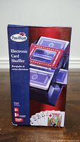 Front of the box showing the Pavilion electronic card shuffler with red top cover and graphic of playing cards.