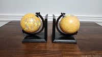 Front view of the globe bookends showing the yellow-toned globes and black bases, displayed on a wooden table.