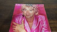 Front cover of Rod Stewart Greatest Hits vinyl record album showing Rod Stewart in bright pink jacket.