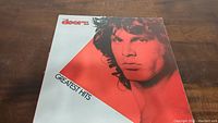 Front cover of The Doors Greatest Hits vinyl album showing Jim Morrison portrait in red tint with band name and album title.