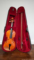 Violin and bow in open case showing the red velvet interior and exterior hard case in black.