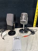 Front view of two desktop microphones showing rectangular silver and black mic on left and vintage chrome style mic on right with audio cables and measuring tape behind.