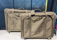 Two olive green vintage Tumi luggage bags side by side, showing front with handles and straps, placed on a white surface with a black background.