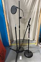 Full view of 3 black adjustable stage microphone stands standing on floor, one with pop filter attached.