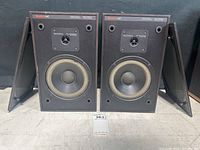 Pair of Boston Acoustic A40 speakers front view showing woofer, tweeter, and wood cases with grille cloths removed and placed behind each speaker.