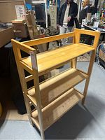 Three-quarter angle view of the assembled collapsible wooden shelf showing three tiers and light wood frame.