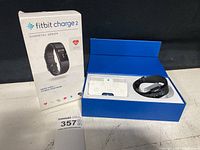 Closed box and open box showing Fitbit Charge 2 packaging and contents including manual and charging cable.