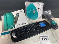 Photo shows Logitech Harmony One remote with USB cable, software CD, instruction manual, and rechargeable battery on white surface.