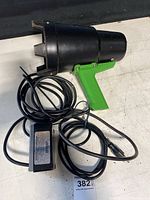 Front and side view of the blacklight inspection device with its green handle, black cylindrical head and attached cables.