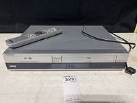Front view of Sony DVD VHS player with remote on top, showing device details and power cord.