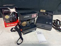 Photo showing Polaroid Sun 660 camera, box, Kodak instant camera with strap, and auction tag