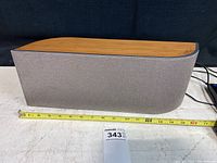 Side view of Wren speaker showing textured gray fabric covering and bamboo wood top, with measuring tape indicating length around 15 inches.