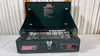 Front view of green Coleman two burner propane stove, showing the burner grates and control knobs.