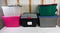 Full view of the six large plastic storage containers stacked in two rows showing various colors and lids.