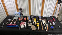 Full overview of the lot including flashlights, paint brushes, rollers, tape, and various hand tools spread on black surface.
