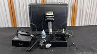 Photo showing the Sunpak Auto 552 Thyristor flash mounted on handle with coiled cord, black carrying case, cleaning blower brush, small bottle, pistol grip, and lens caps spread on a surface