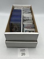 Two-row white cardboard box filled with basketball cards, most in plastic sleeves for protection.