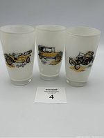 Three frosted glasses side by side showing vintage car illustrations and labels in black and yellow tones.