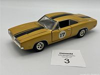 Angle view of gold die cast 1969 Dodge Charger R/T model including black stripes and number 17 decal on door.