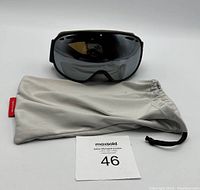 Front and side view of Bollé goggles with storage bag on white background, showing tinted reflective lens and foam padding inside frame.