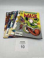 Nine comic books stacked showing front covers with different colorful artworks of The Mask character.