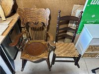 Lot of two vintage rocking chairs shown side by side. One has carved details and leather seat, other has ladder back and woven seat with broken spindle.