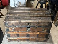 Front view of vintage trunk showing metal lock, metal straps, handles and wood slats with wear