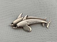 Top-down view of the dolphin sterling silver brooch showing details of dolphins and markings.