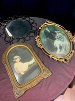 Three antique items displayed together: black wrought iron round mirror, wooden ornate photo frame with child portrait, and oval brass photo frame with wedding photo