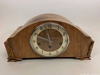 Front view showing clock face with Arabic numerals and wooden carved details on sides.