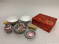 Miniature porcelain rice bowls, cloisonné bud vase, cloisonné egg, small cloisonné box, and red silk brocade box shown together