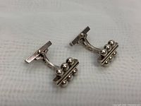 Front view of both cufflinks showing rectangular bar and three silver spheres.