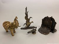Overview photo showing all four items in the lot: brass elephant, mallard duck sculpture, old genie oil lamp, and peacock bookends.