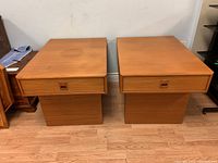 Front view of pair of teak side tables showing drawers and pedestal bases