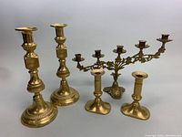 Pair of 12-inch and 6-inch brass candleholders alongside a five-arm brass candelabra showing overall set composition