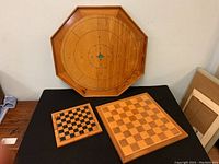 Full view of vintage octagonal crokinole board with two wooden checker boards on black table, showing size and wear.