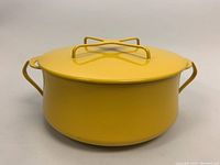 Front view of a round yellow enamel covered pot with handles on both sides and a fitted lid with a raised X handle.
