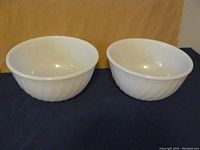 Two white swirl pattern glass bowls side by side on a dark surface with beige background.